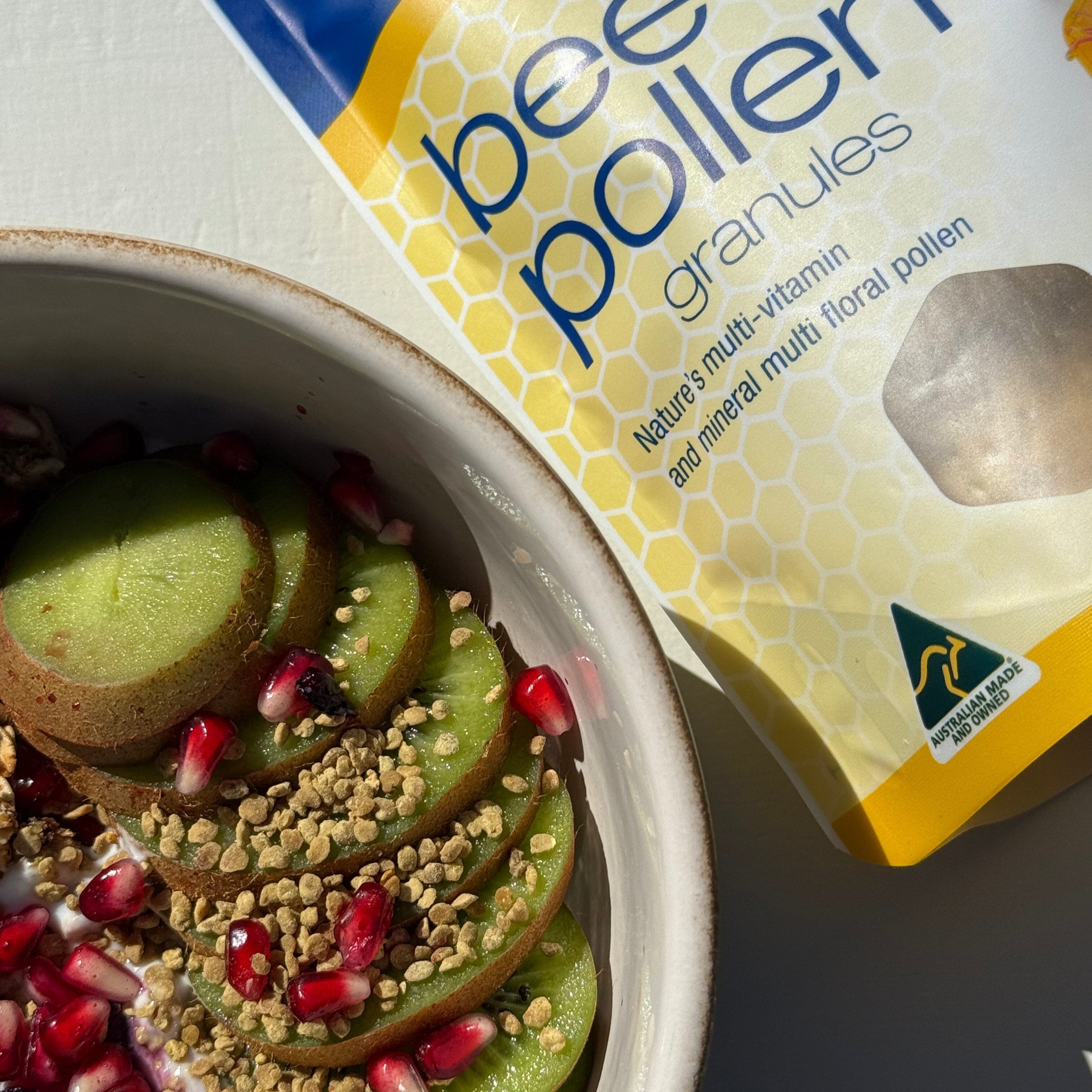 Bowl of kiwi slices with pomegranate seeds next to a package of Bee Pollen Granules.