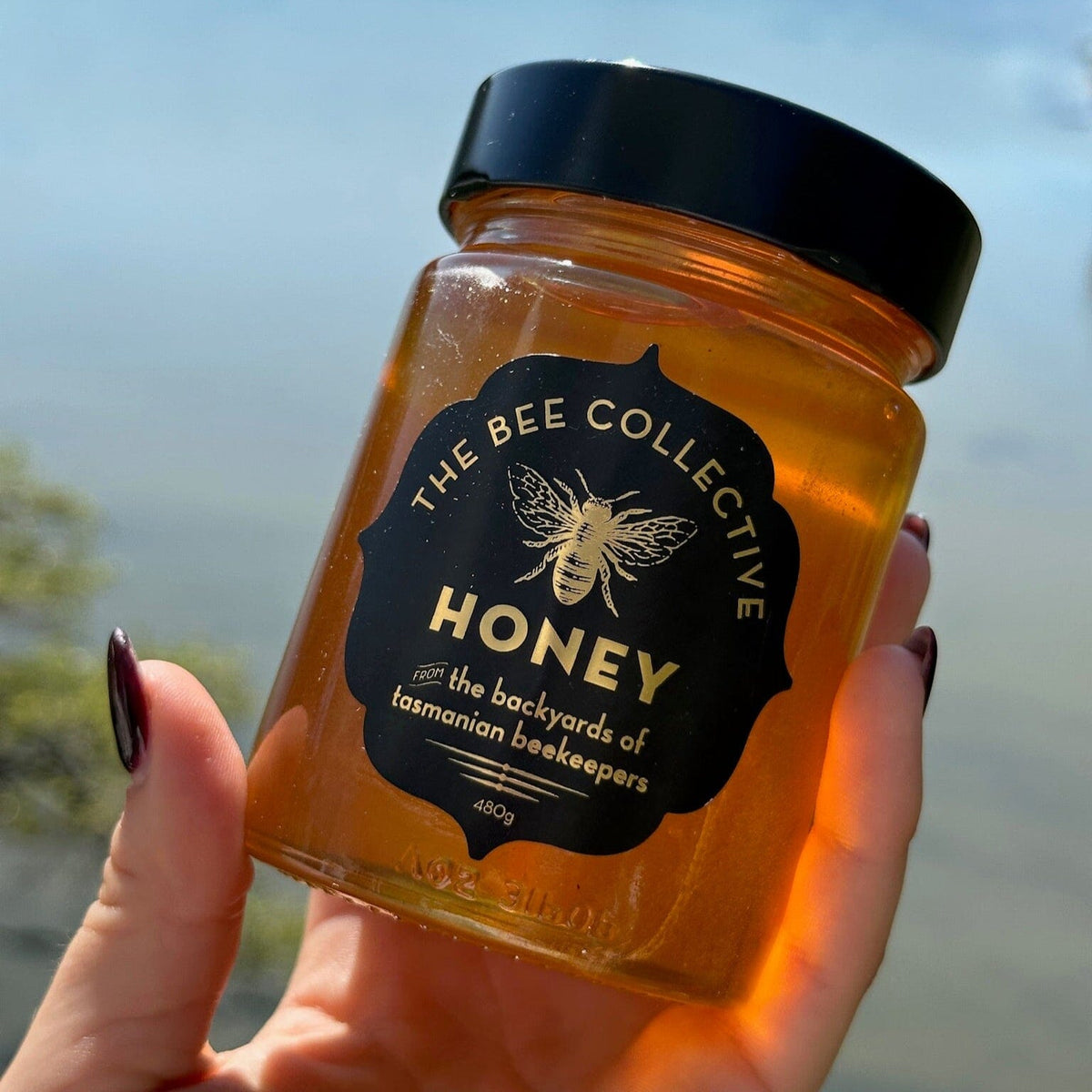 Jar of honey from The Bee Collective held in front of a blurred natural background