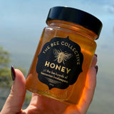 Jar of honey from The Bee Collective held in front of a blurred natural background