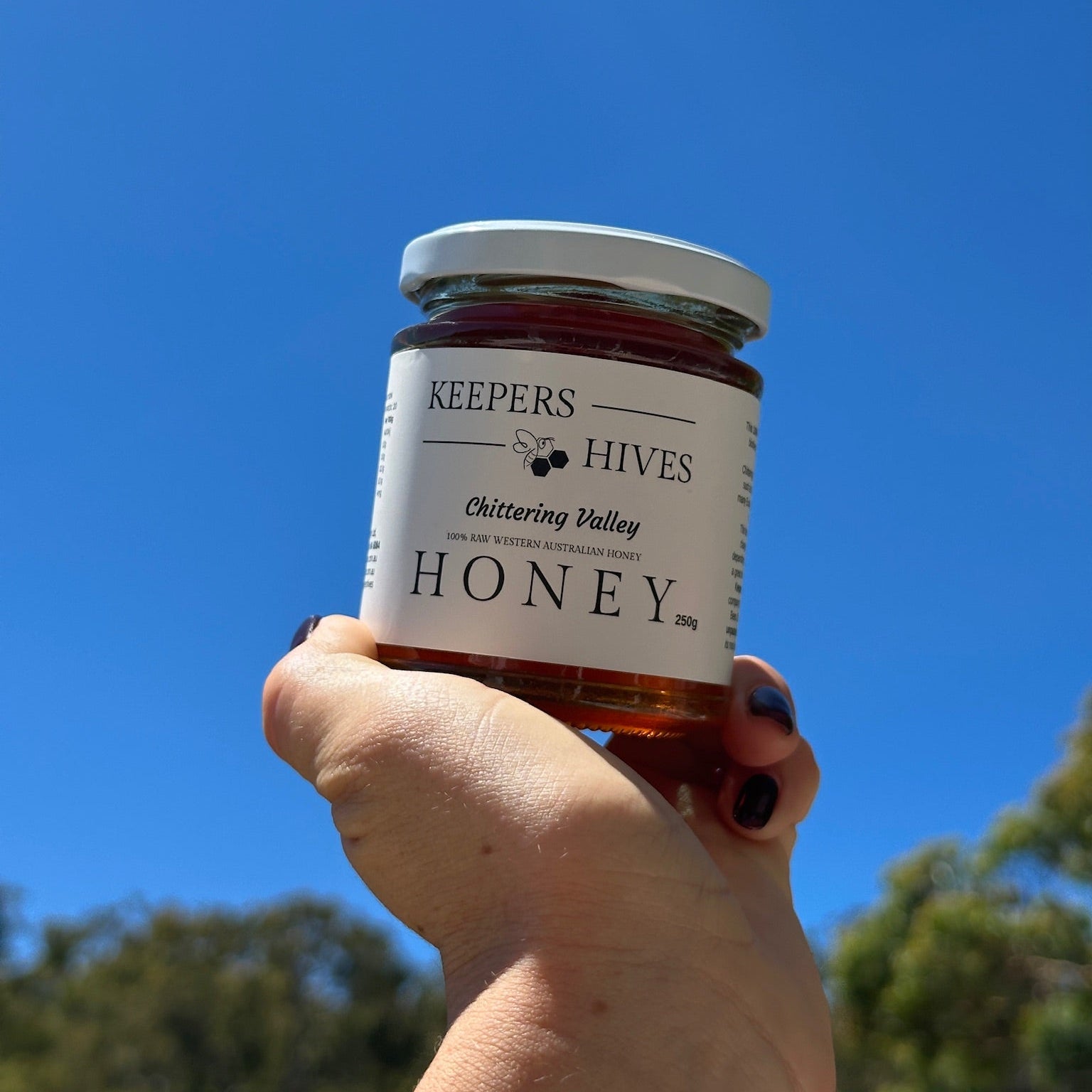Jar of 'Keepers Hives' honey held against a clear blue sky