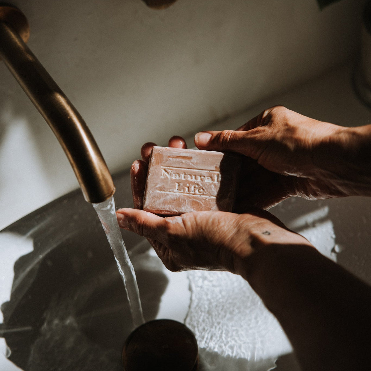 Person holding a bar of Natural Life Propolis & Manuka Honey soap above a sink with water running.
